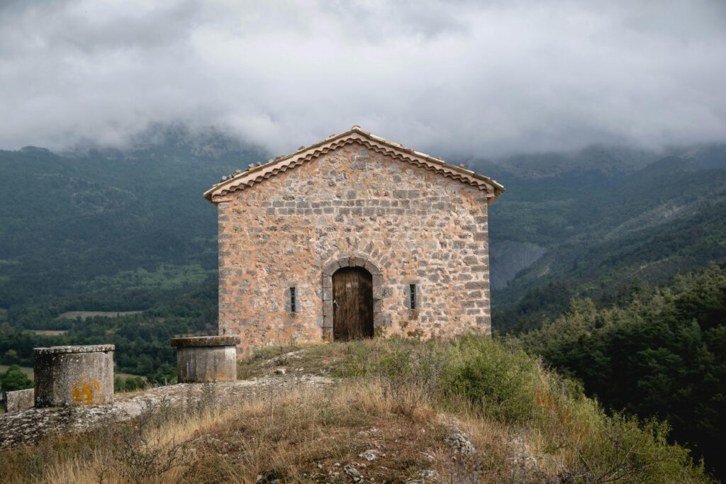 Stone building in Vergons, France, surrounded by lush mountains under a cloudy sky.